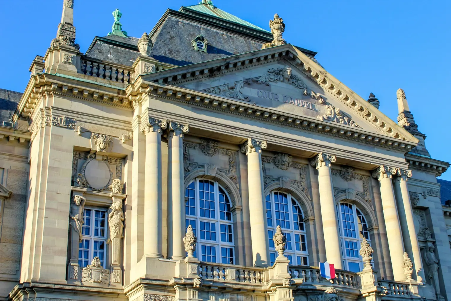 Façade ornée d’un bâtiment public, un drapeau français au balcon.